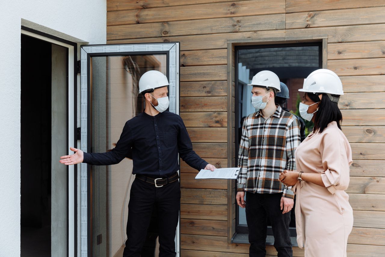 Real estate agent with clients viewing a new house during COVID-19 wearing safety gear.